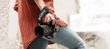 Close up image of a person carrying a camera in their right hand whilst casually walking up stairs with the FE 16-35mm F2.8 GM lens mounted