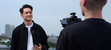 Usage image of a man hand-holding a camera, shooting footage of another man with an ECM-L1 microphone in an outdoor setting