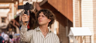 Usage image of a man holding a grip attached to the camera in his right hand, filming himself walking down the street