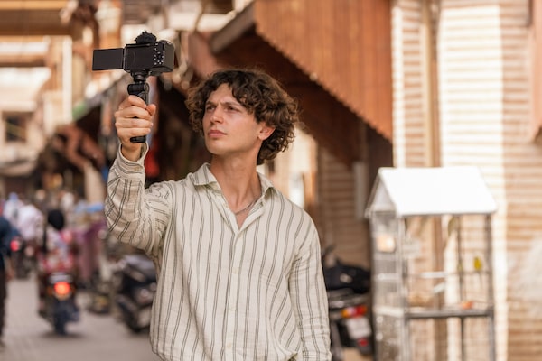 Usage image of a man holding a grip attached to the camera in his right hand, filming himself walking down the street