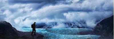 Image showing user holding camera in wild mountainous environment with mist, clouds, and glacial ice field